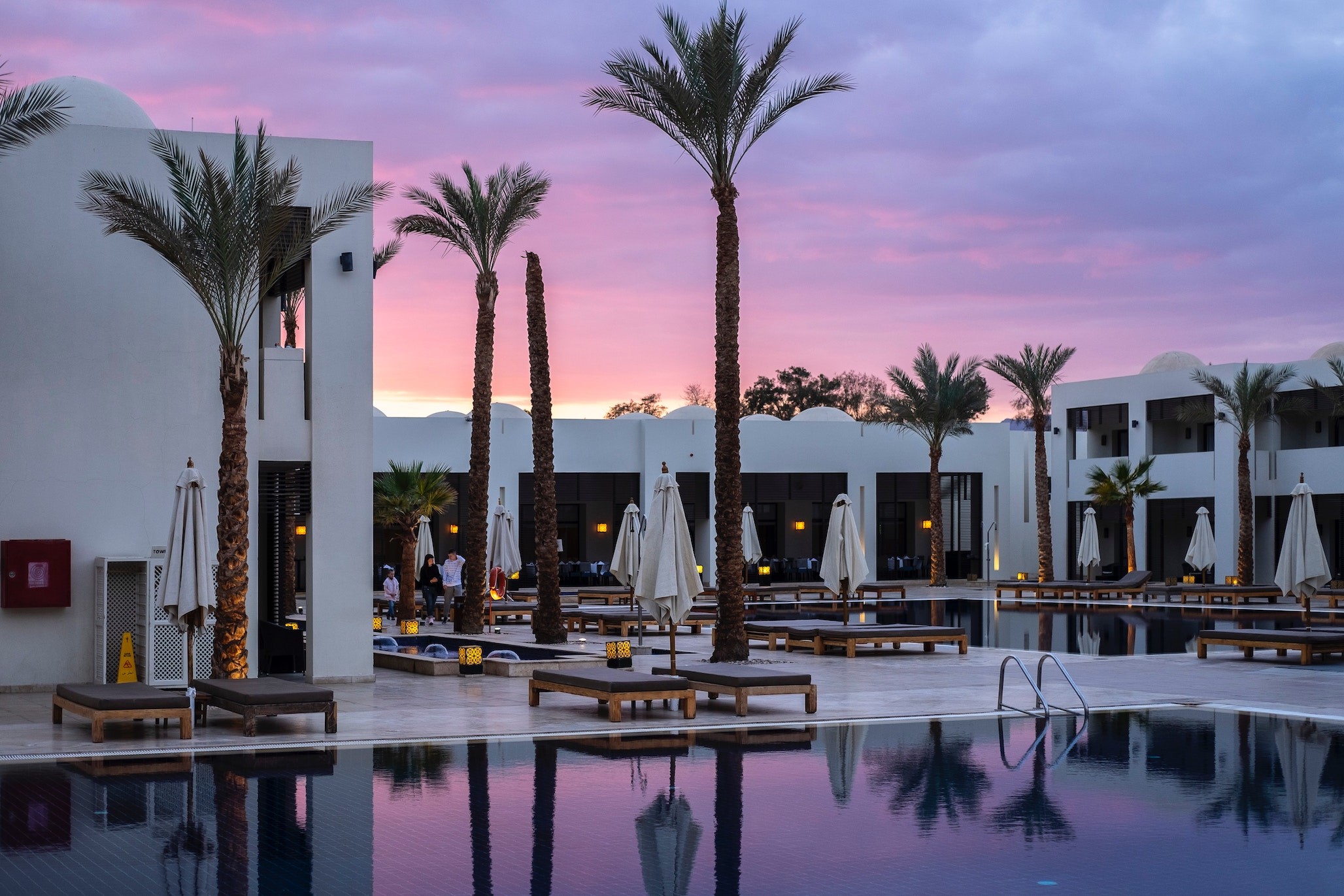 A hotel pool at dusk with lounge chairs
