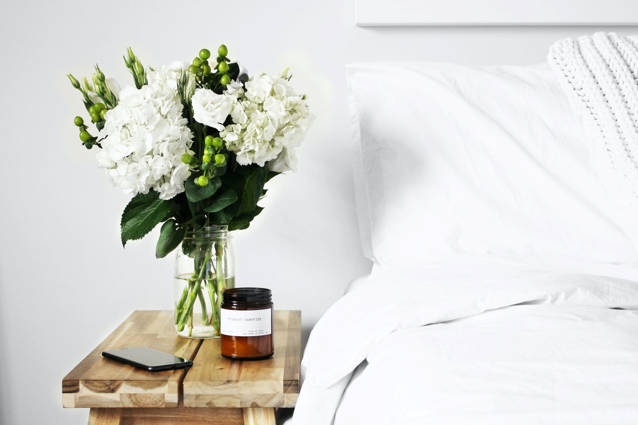 An Airbnb bedside table with a vase of white flowers and a phone.