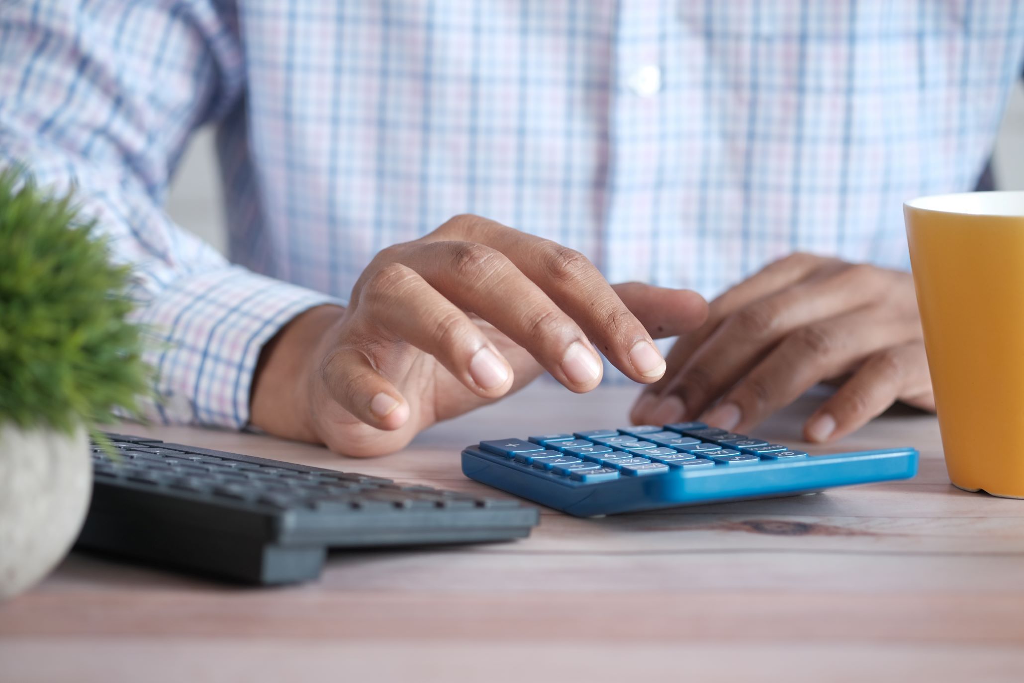 A Man Is Using A Calculator Instead of Hotel Revenue Management Software on a Desk with a Cup